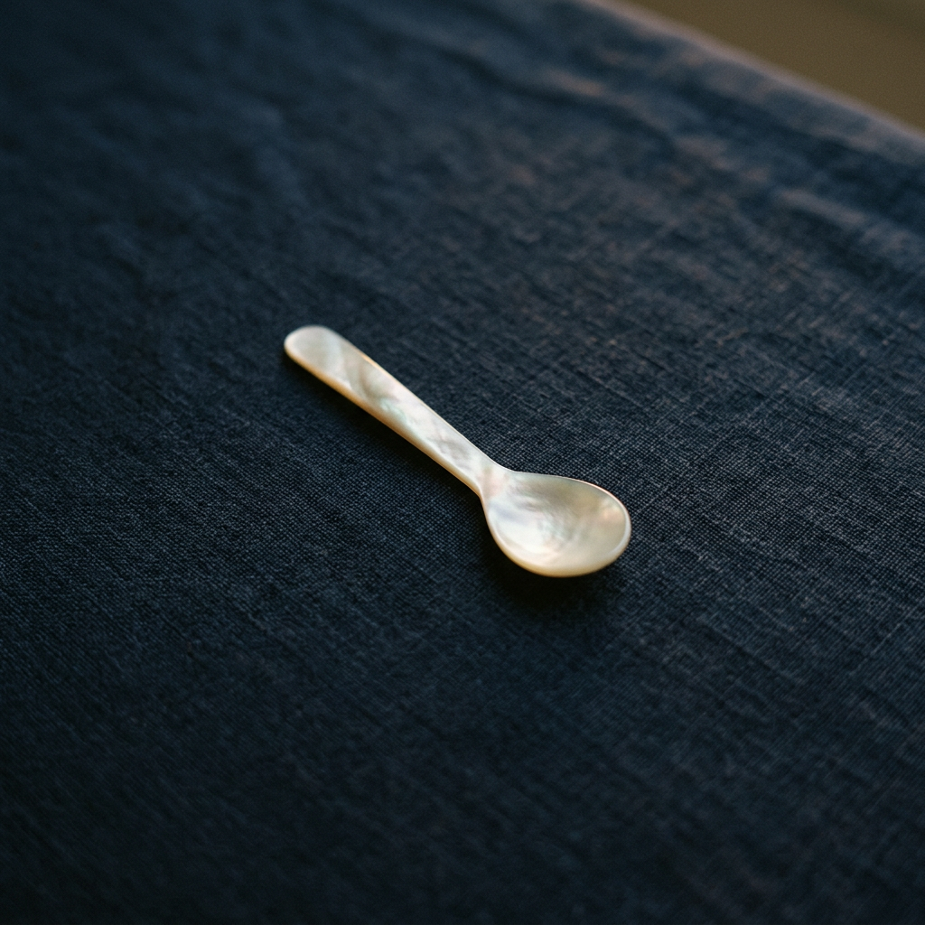A single mother-of-pearl caviar spoon photographed alone on dark navy linen, soft highlights catching the iridescent sur